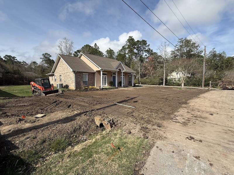 Front yard of a brick house graded down to bare dirt, with an orange track loader parked by the house