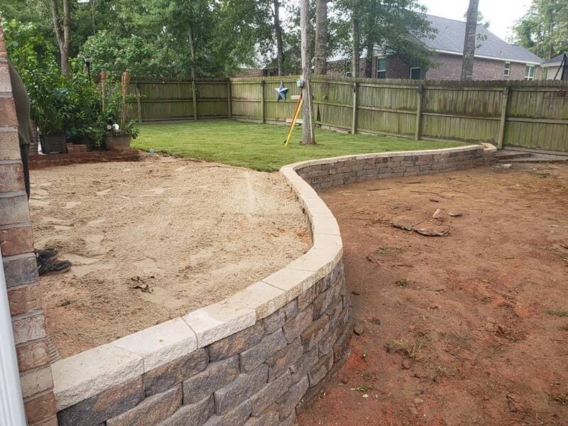 Curved block retaining wall with light caps holding a raised sand bed, with new sod and a wood fence behind it