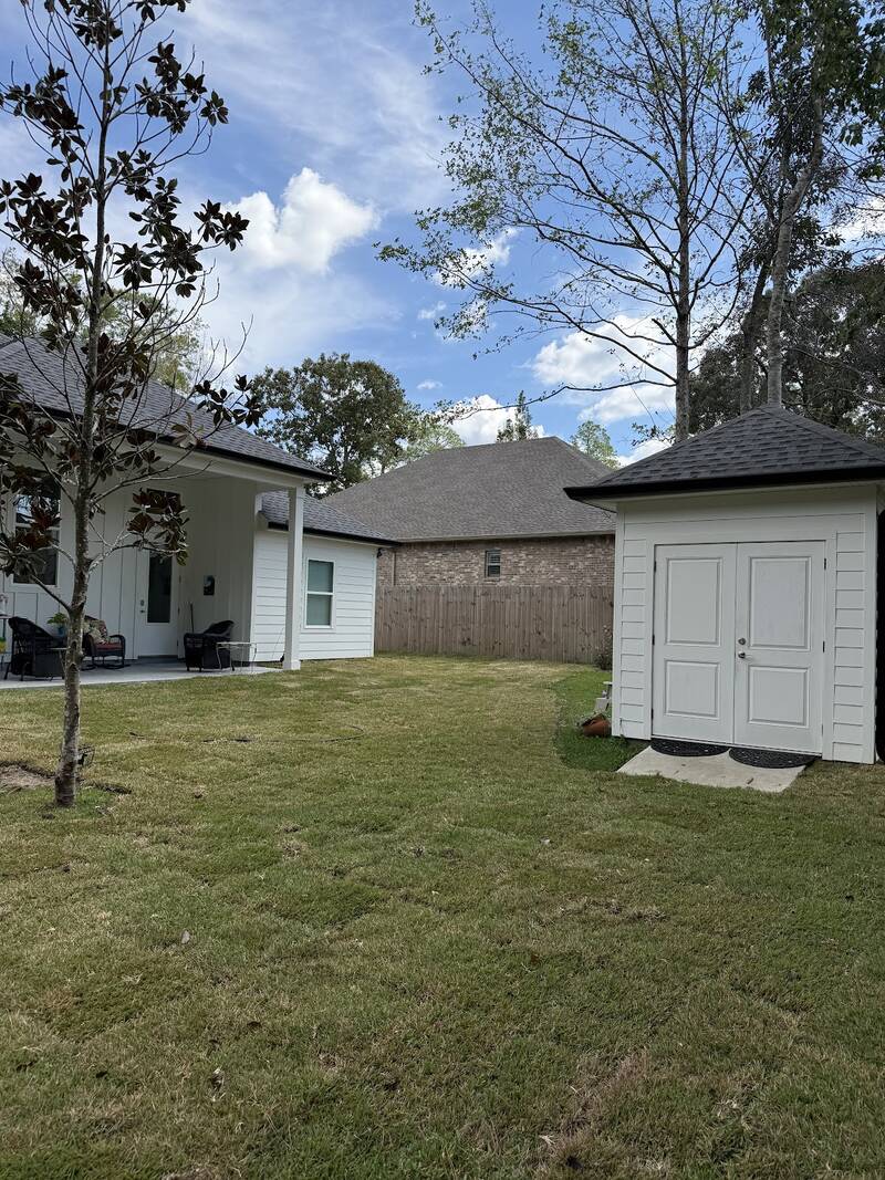 Fresh green sod across the backyard of a white house with a covered patio and a white shed